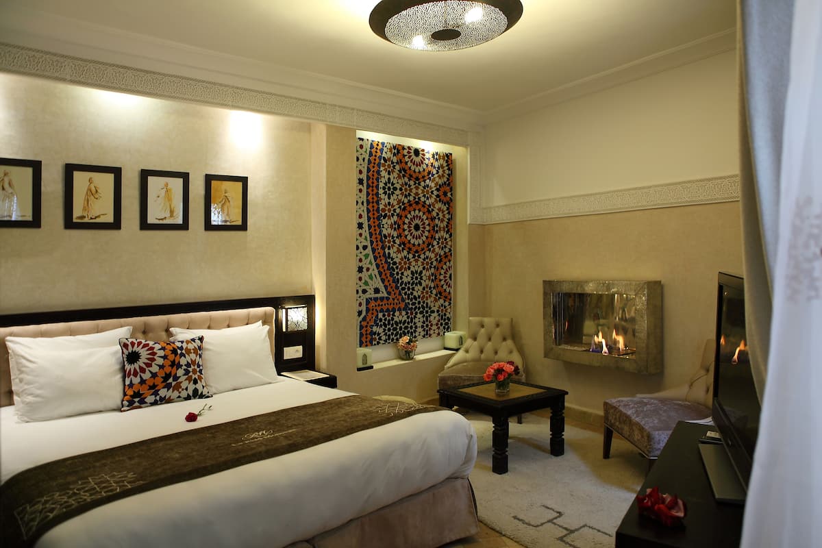 A hotel room with a large bed, a fireplace, a TV, and a decorative wall tapestry.