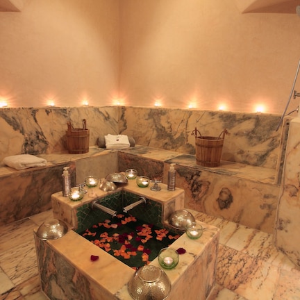 A spa room with a marble bathtub, candles, and rose petals.