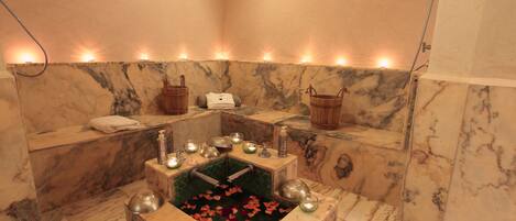 A spa room with a marble bathtub, candles, and rose petals.