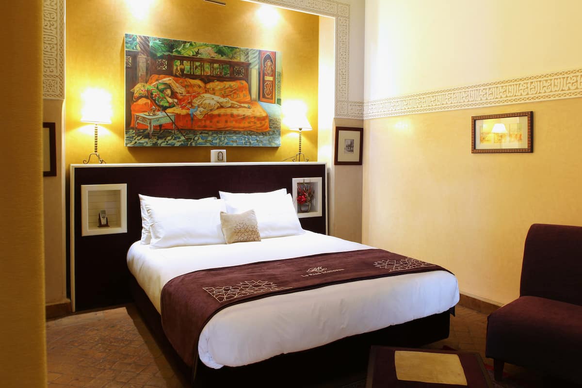 A hotel room with a large bed, a chair, a painting on the wall, and two lamps.