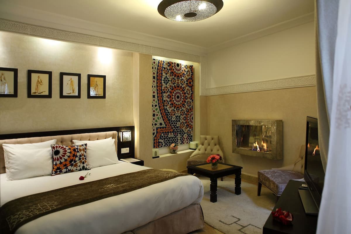 A hotel room with a bed, a TV, a fireplace, and artwork on the walls.