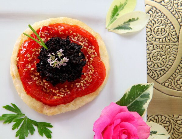A dessert with a red topping, sesame seeds, and a green garnish on a white plate.