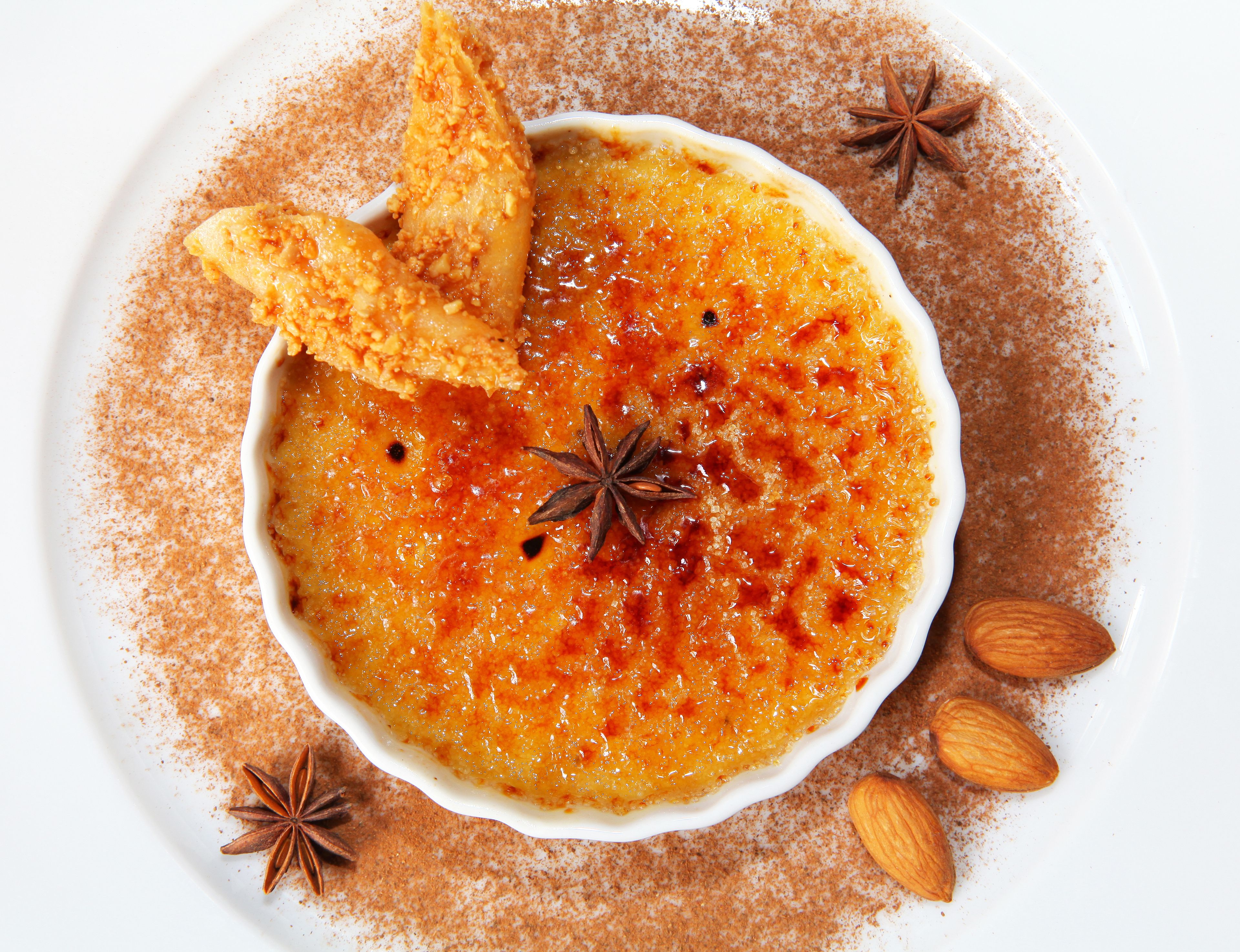 Eine Schale Crème Brûlée, verziert mit Zimt und Sternanis, zusammen mit Mandeln und einem Stück Brot.