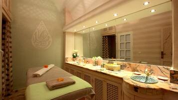 Ett spa-rum med en massagebänk, en stor spegel och ett handfat i marmor.