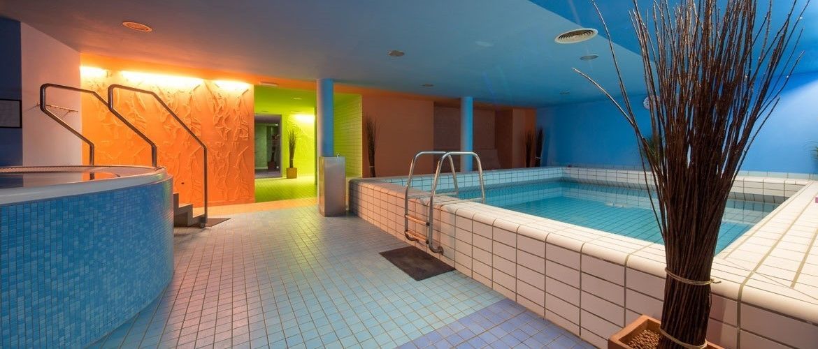 A swimming pool area with a hot tub, a water feature, and a staircase leading to a balcony.