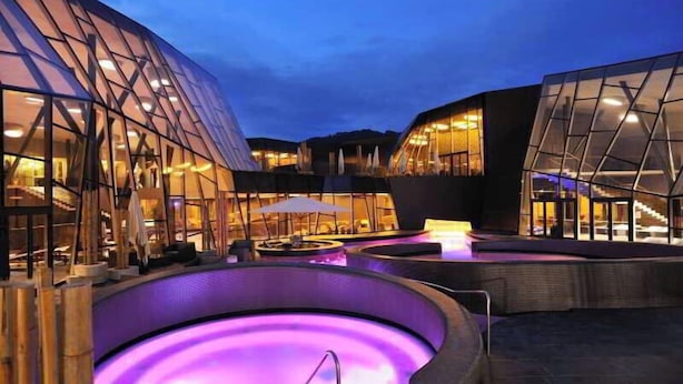 Un edificio moderno con fachadas de vidrio y un área de piscina exterior climatizada.