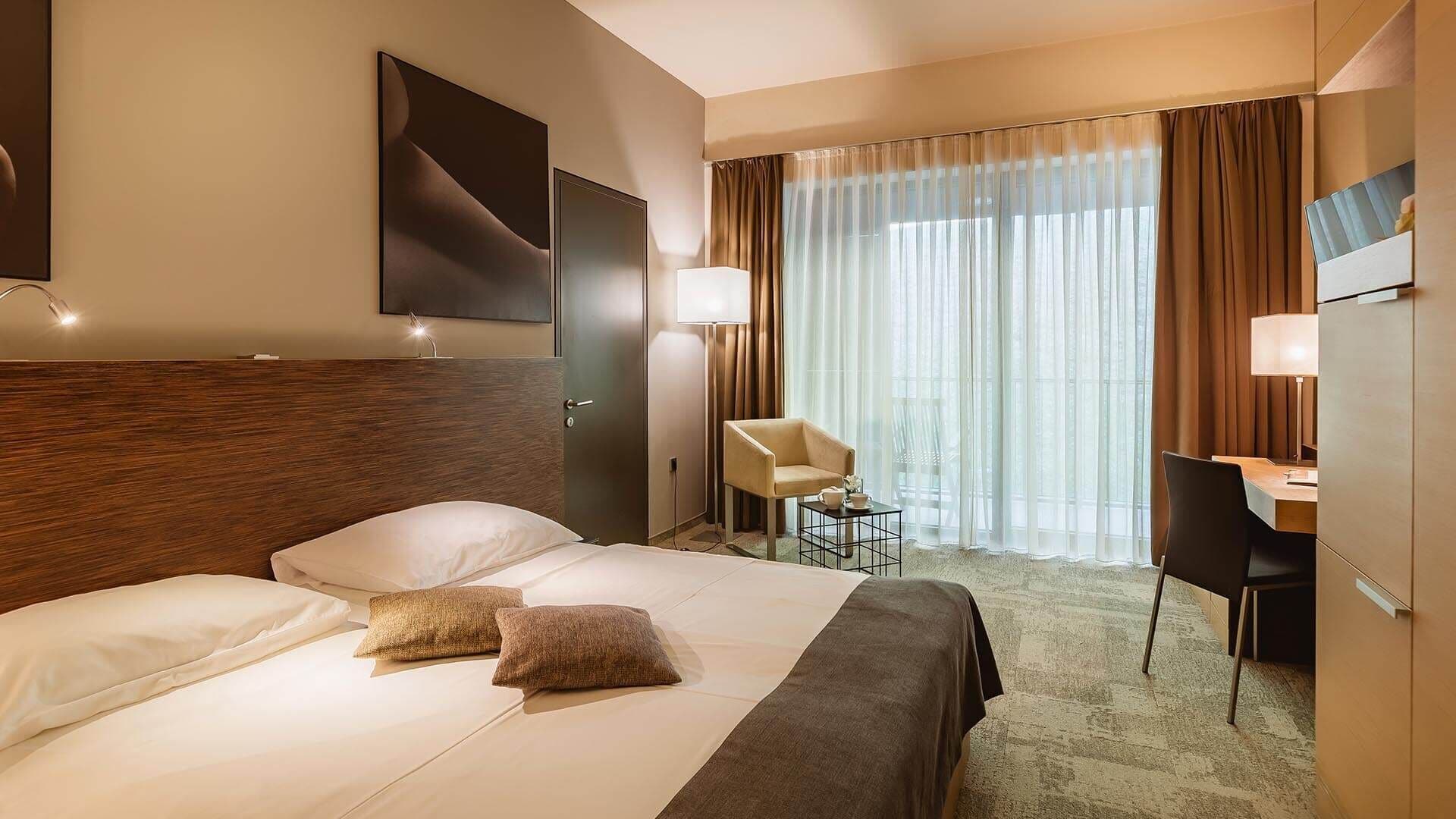 Een hotelkamer met een bed, bureau, stoel, televisie en een raam met gordijnen.