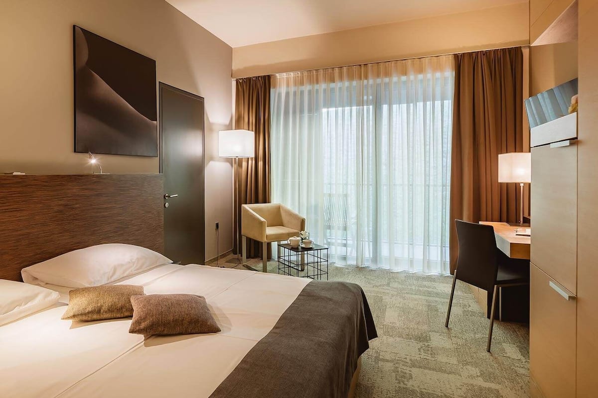 Une chambre d’hôtel avec un grand lit, un bureau, une chaise, une télévision et une fenêtre avec des rideaux.
