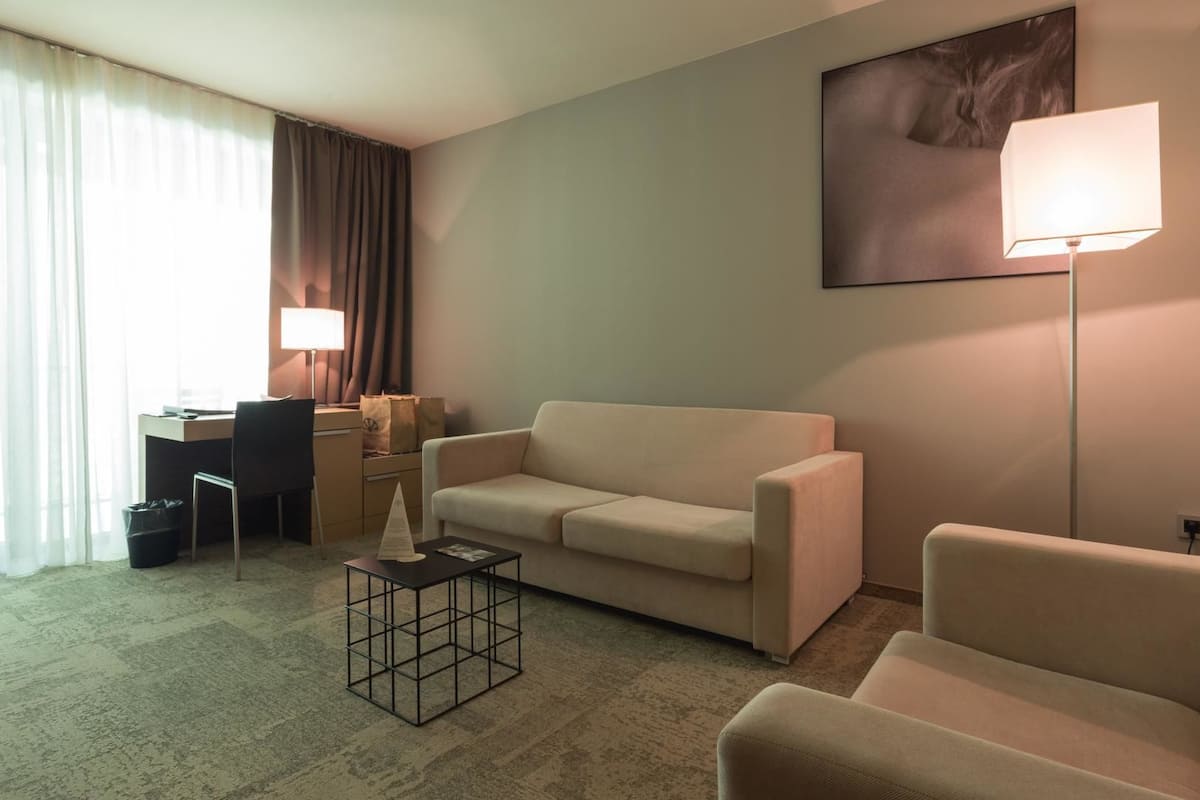 Une chambre d’hôtel équipée d’un canapé, d’un fauteuil, d’un bureau, d’une lampe et ornée d’un tableau au mur.