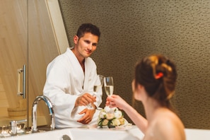 Um homem de batina sentado à mesa com uma mulher, ambos segurando copos de vinho.
