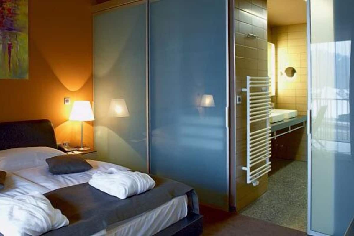 Une chambre d’hôtel avec un lit, une table de chevet, une lampe, une salle de bain avec un porte-serviettes et un tableau au mur.