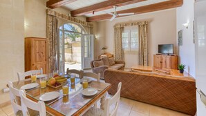 A dining area with a glass table, chairs, and a buffet with fruits and drinks. There is a sofa and a television in the background. - Villagg Tal Fanal (Ghasri)