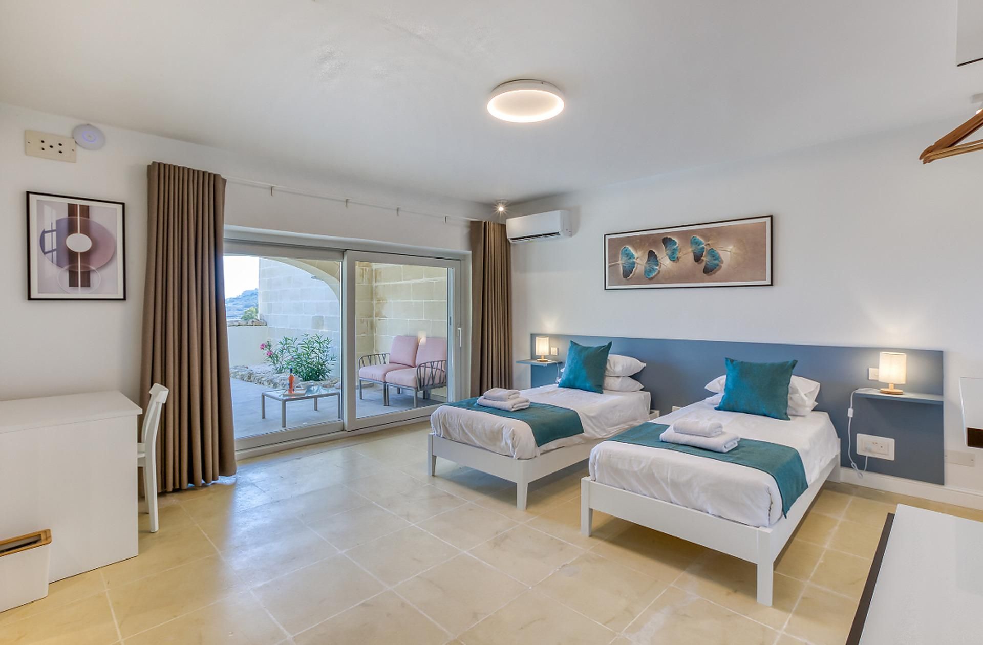 Una camera d'albergo con due letti, un balcone e vista sull'esterno.