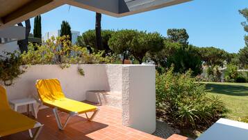 A patio with two yellow lounge chairs, a white table, and a white chair.