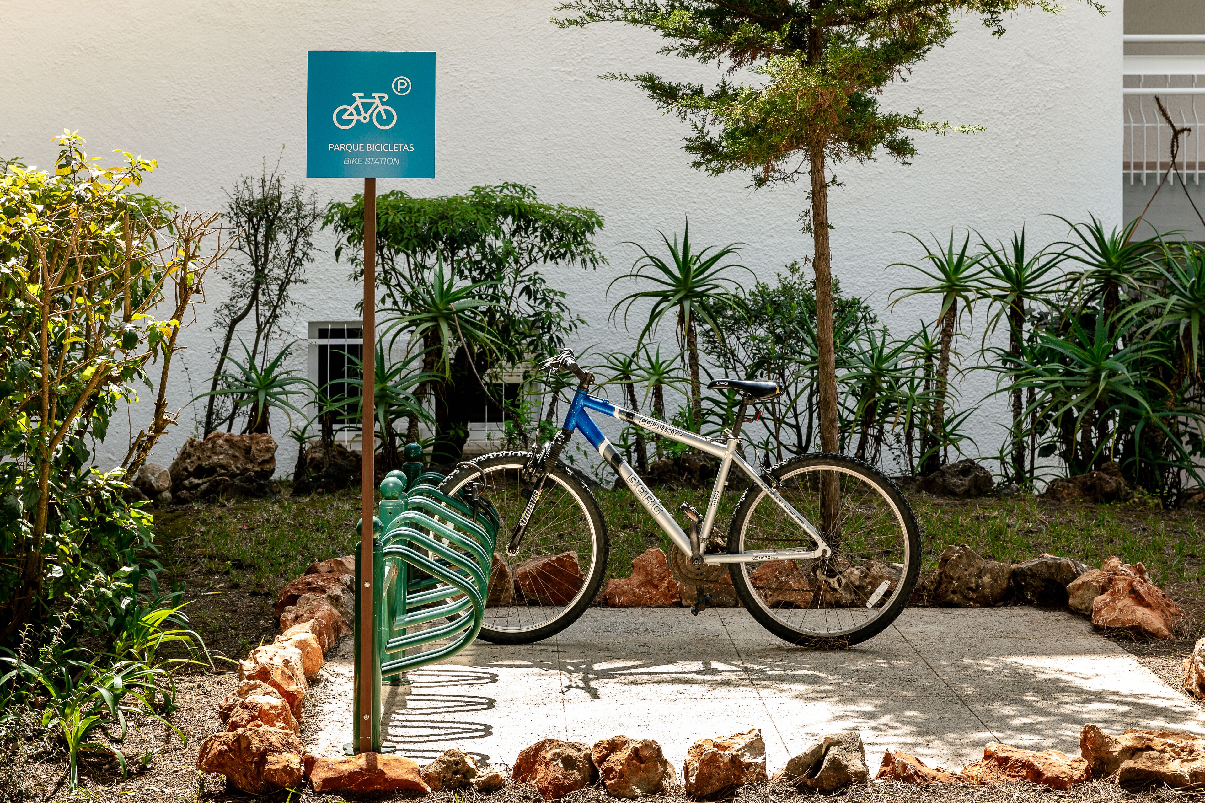 A bicycle parked near a bike station sign, surrounded by rocks and plants.
