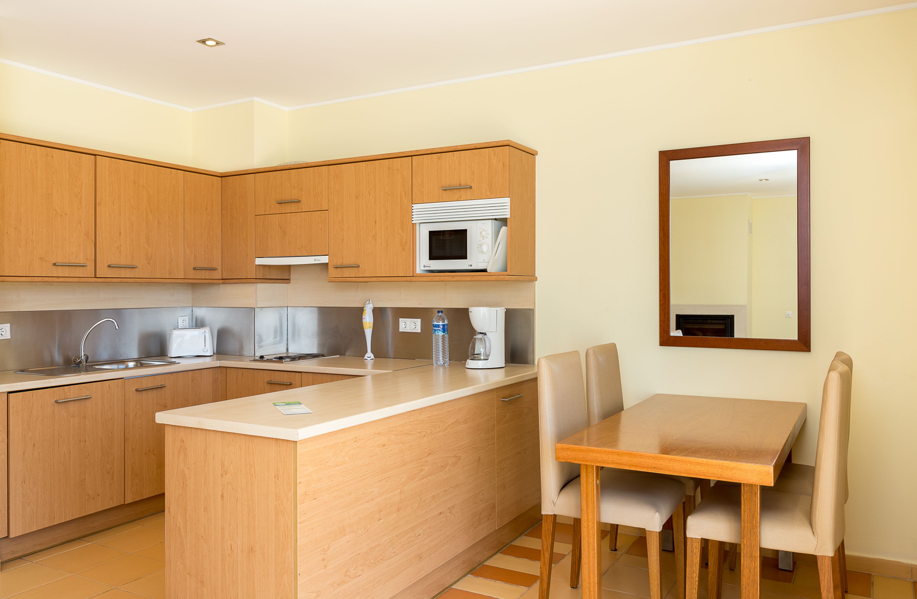 A modern kitchen with wooden cabinets, a microwave, a coffee maker, and a dining area with a table and chairs.