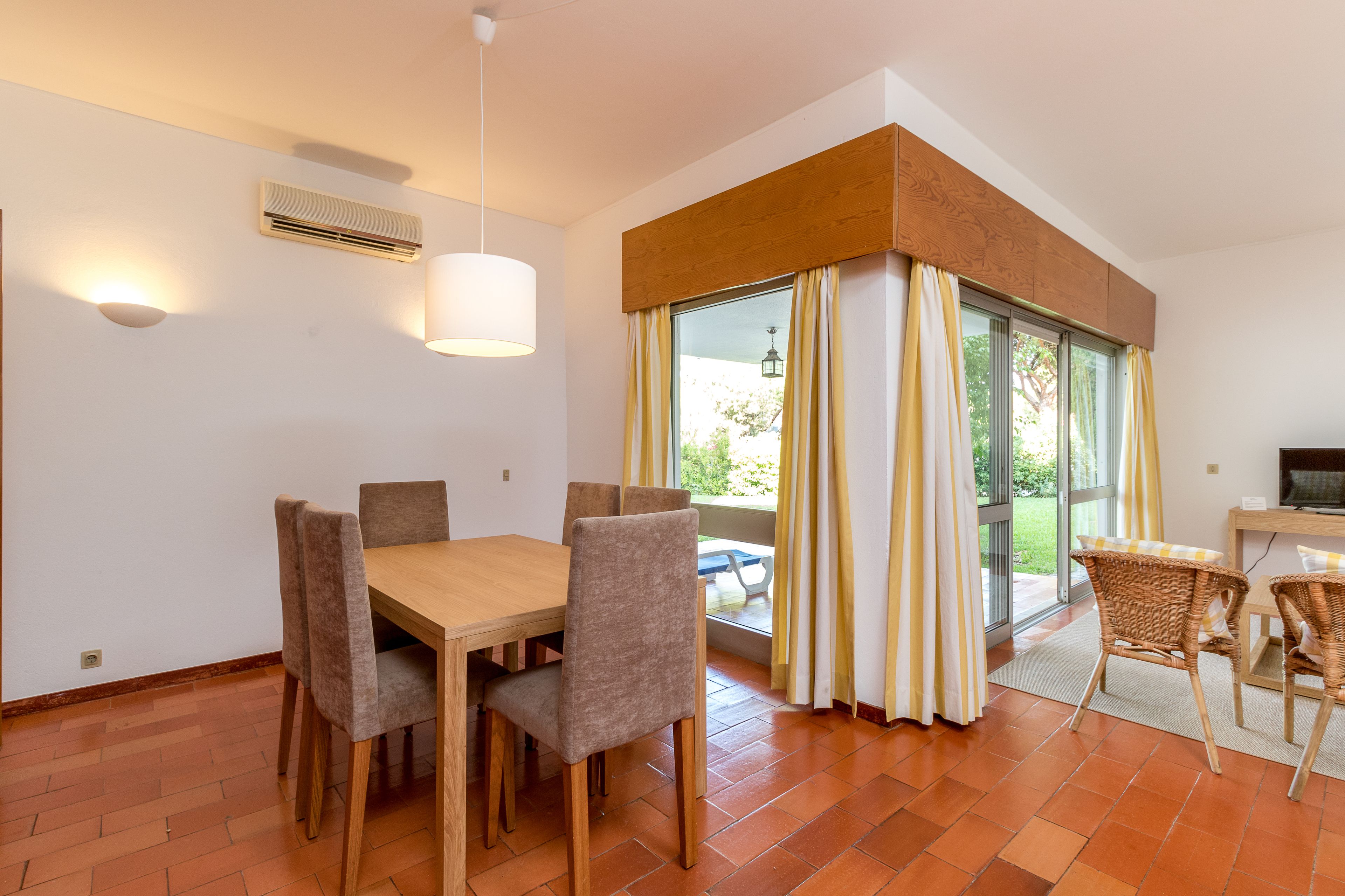 A dining area with a table and chairs, a ceiling light, and a view through a window with curtains.