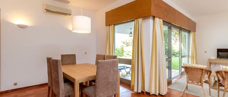 A dining area with a table and chairs, a ceiling light, and a view through a window with curtains.