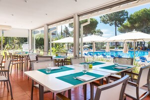 A restaurant with outdoor seating overlooking a pool, featuring tables with green placemats and white tablecloths.