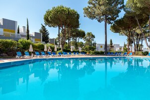 Una piscina con sillas de descanso azules y sombrillas, rodeada de árboles y edificios.