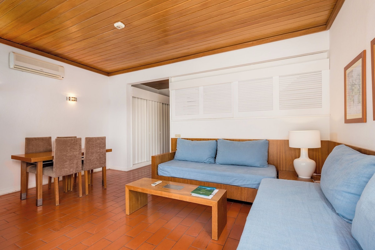 A modern living room with a wooden ceiling, a sofa, a coffee table, and a dining area with chairs.