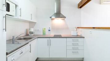 Une cuisine compacte avec des meubles blancs, une hotte de cuisinière en acier inoxydable, un four à micro-ondes encastré et une machine à café.