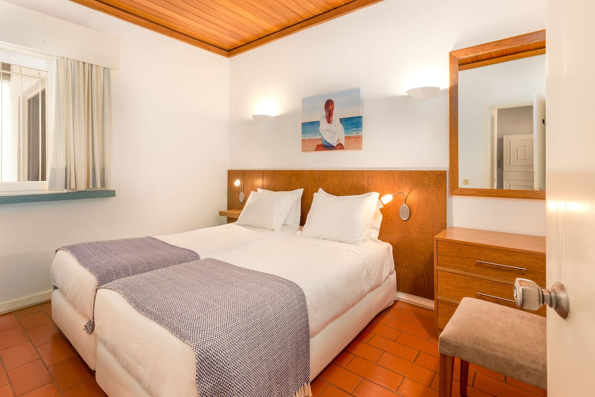 A hotel room with a large bed, a wooden headboard, a bedside table, a mirror, and a painting of a beach scene.
