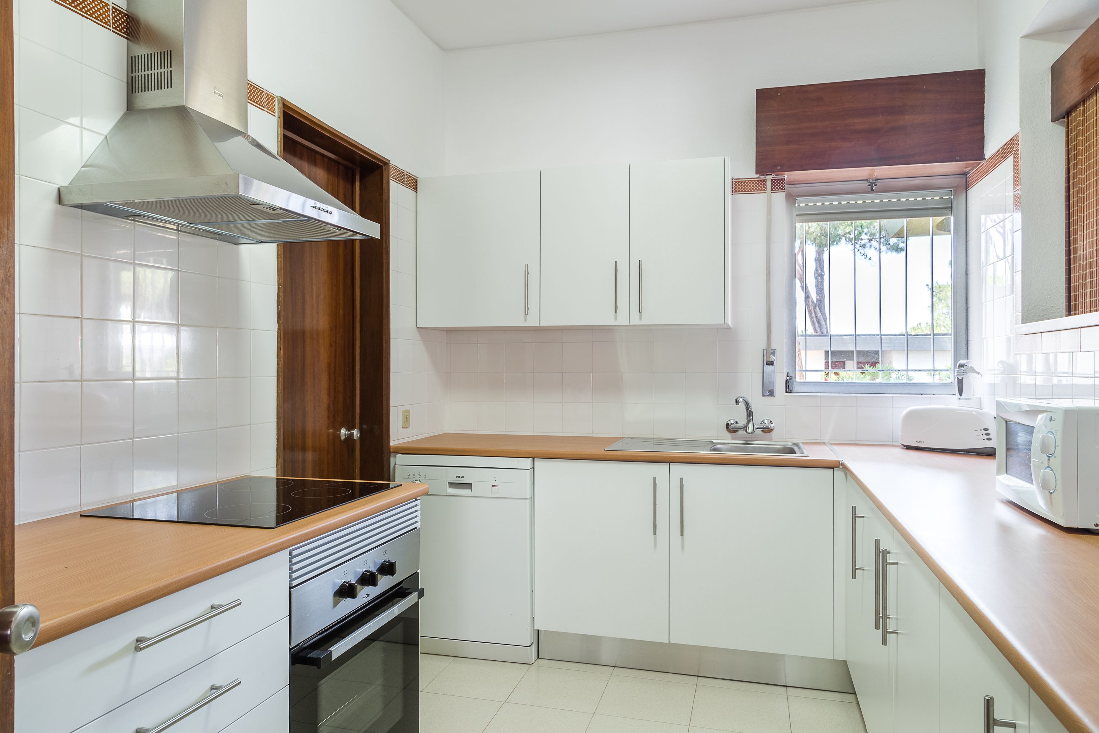 A kitchen with white cabinets, a wooden countertop, a built-in oven, a dishwasher, and a window with a view.