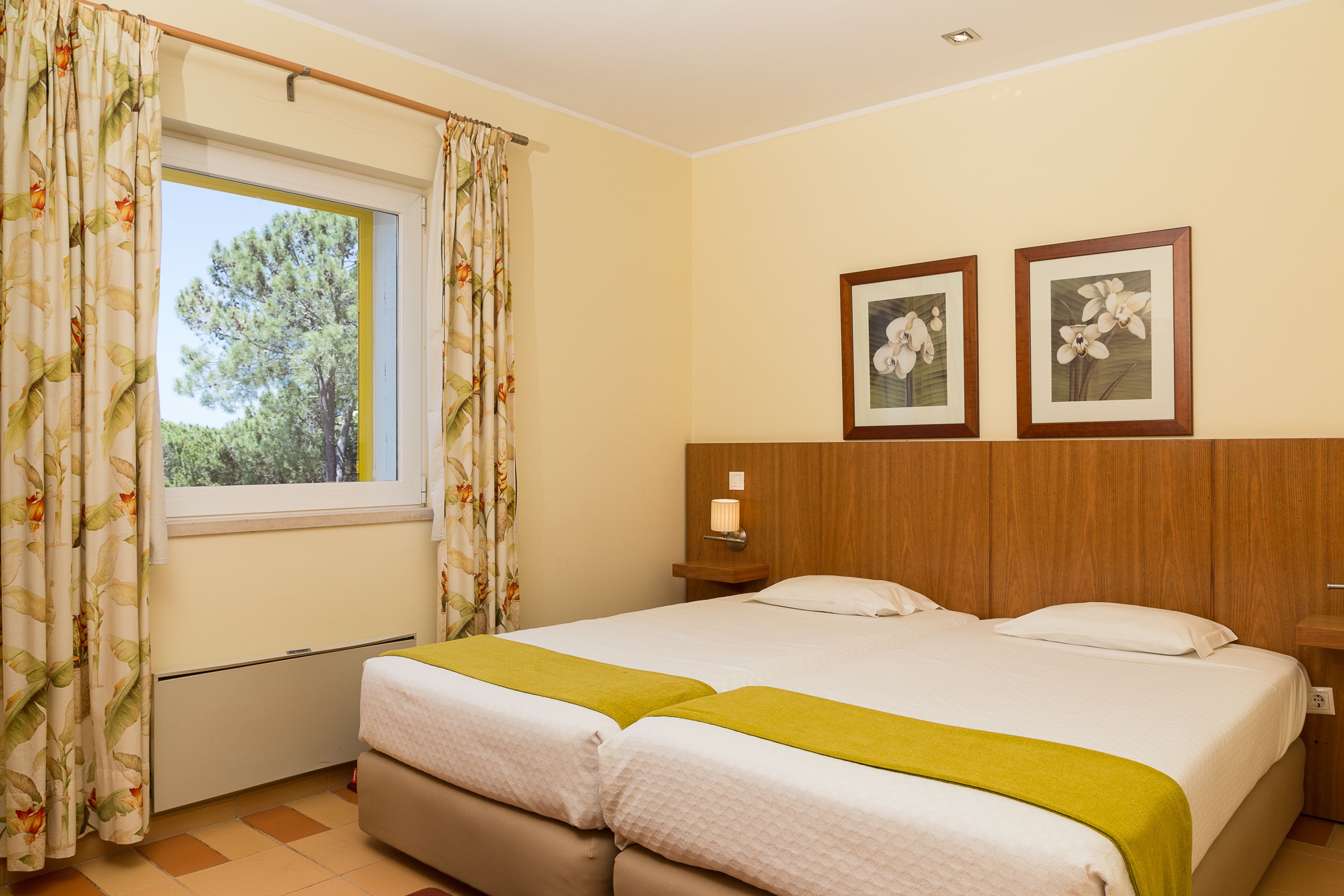 A double bed with a green throw, a wooden headboard, and two framed floral pictures on the wall.