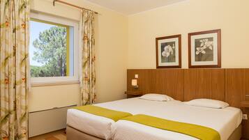 A double bed with a green throw, a wooden headboard, and two framed floral pictures on the wall.