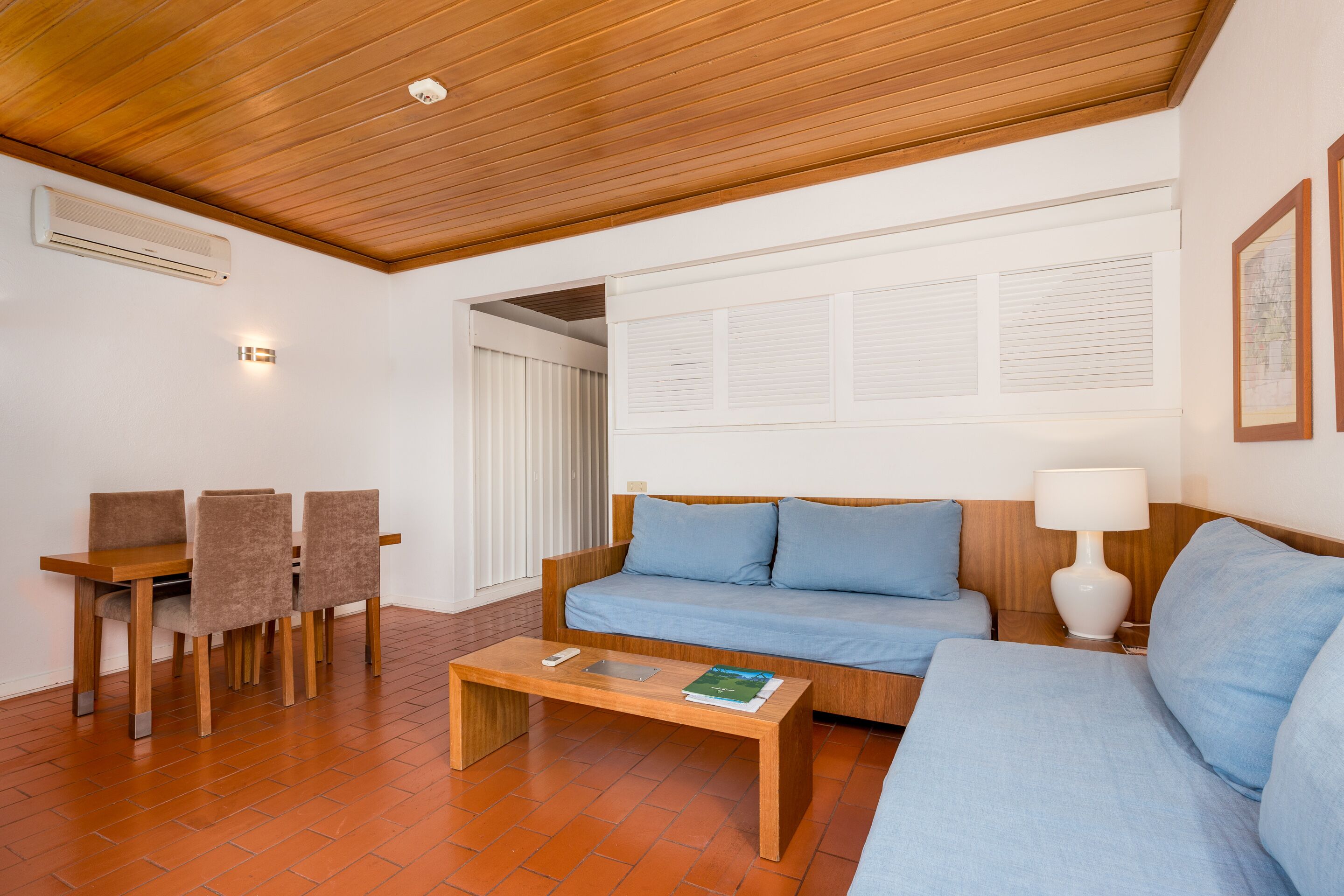 Ein modernes Wohnzimmer mit Holzbalkendecke, einer Couch, einem Couchtisch und einem Essbereich mit Stühlen.