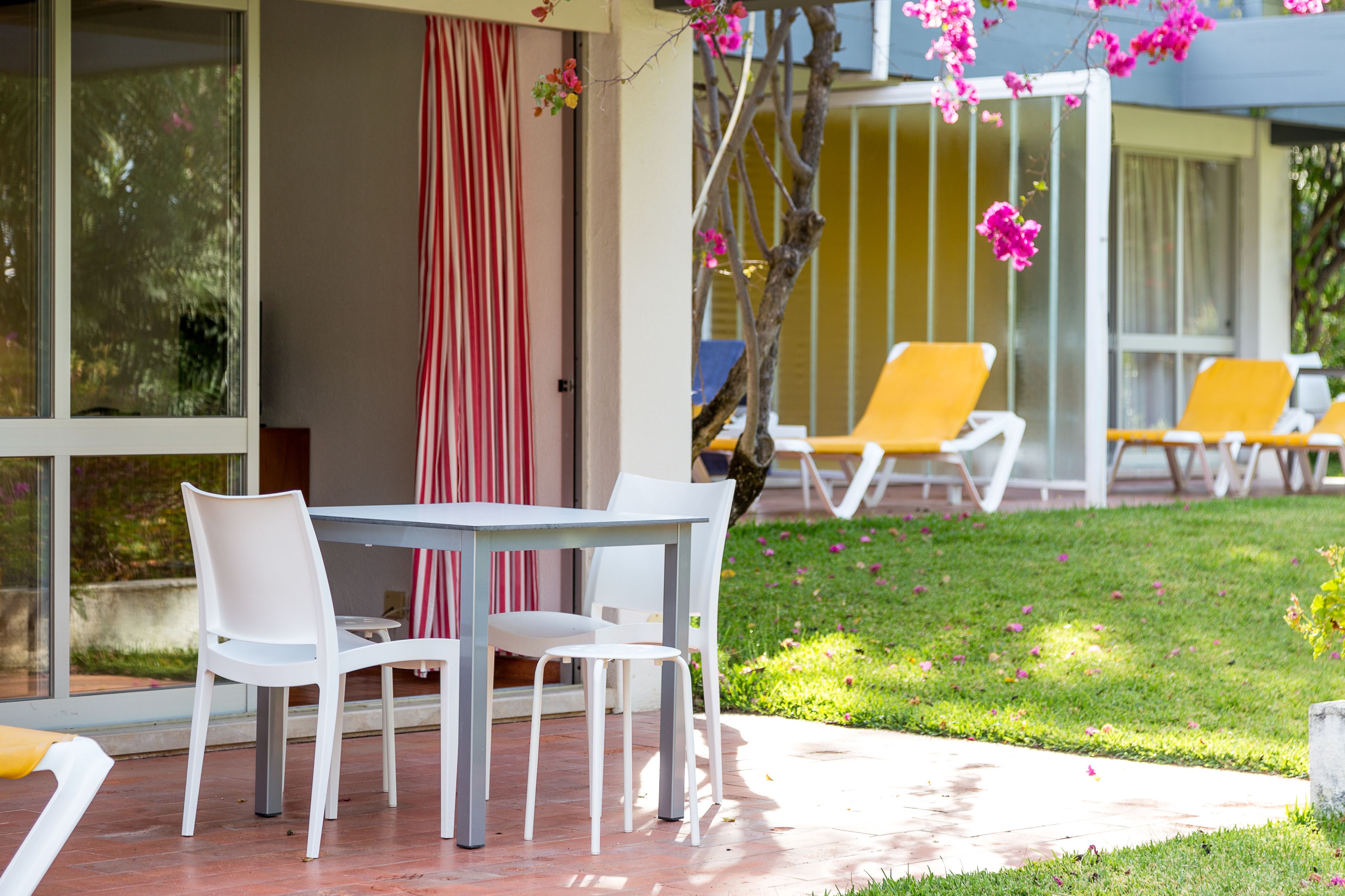 An outdoor seating area with a table and chairs, a grassy lawn, and a building in the background.