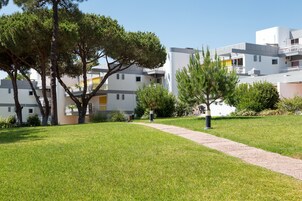 Ένα σύγχρονο κτίριο κατοικιών με ένα μονοπάτι που οδηγεί στην είσοδο, το οποίο περιβάλλεται από καλά συντηρημένο γρασίδι και δέντρα.