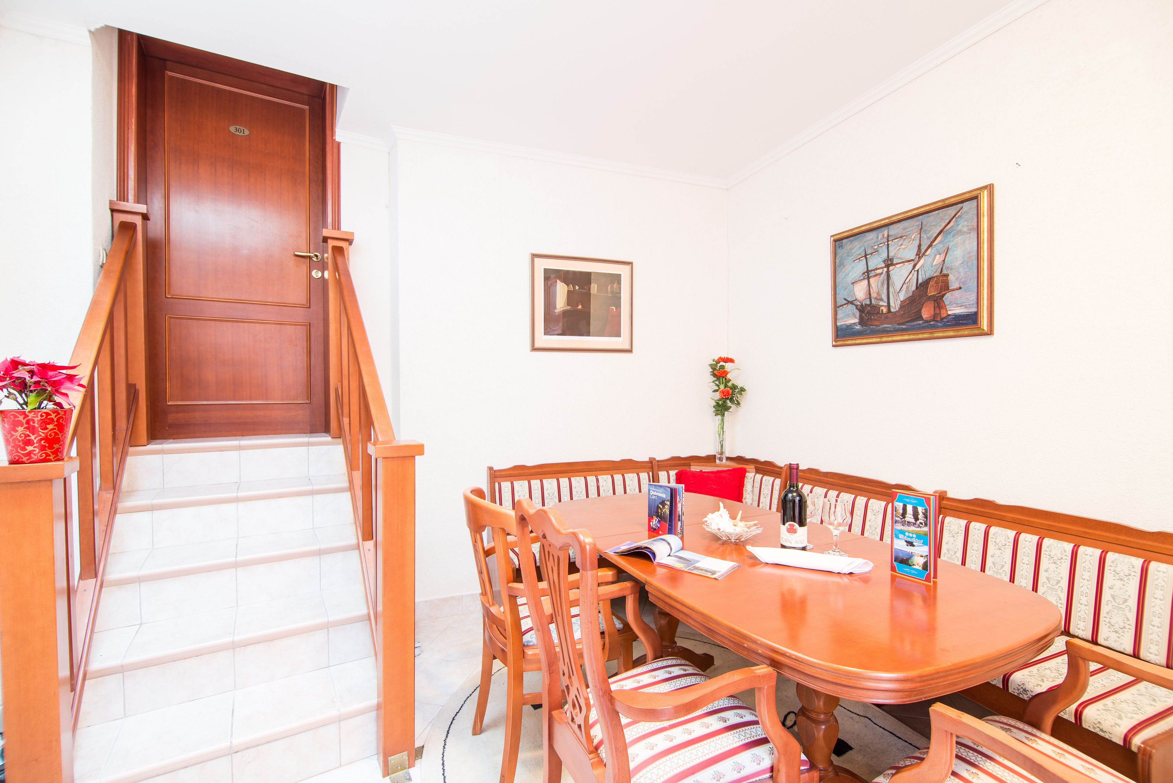 A dining area with a wooden table, chairs, and a bench. There is a staircase leading to an upper floor.