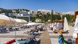 A beachside area with sun loungers, umbrellas, and a wooden walkway. - Hotel Dubrovnik (Dubrovnik)
