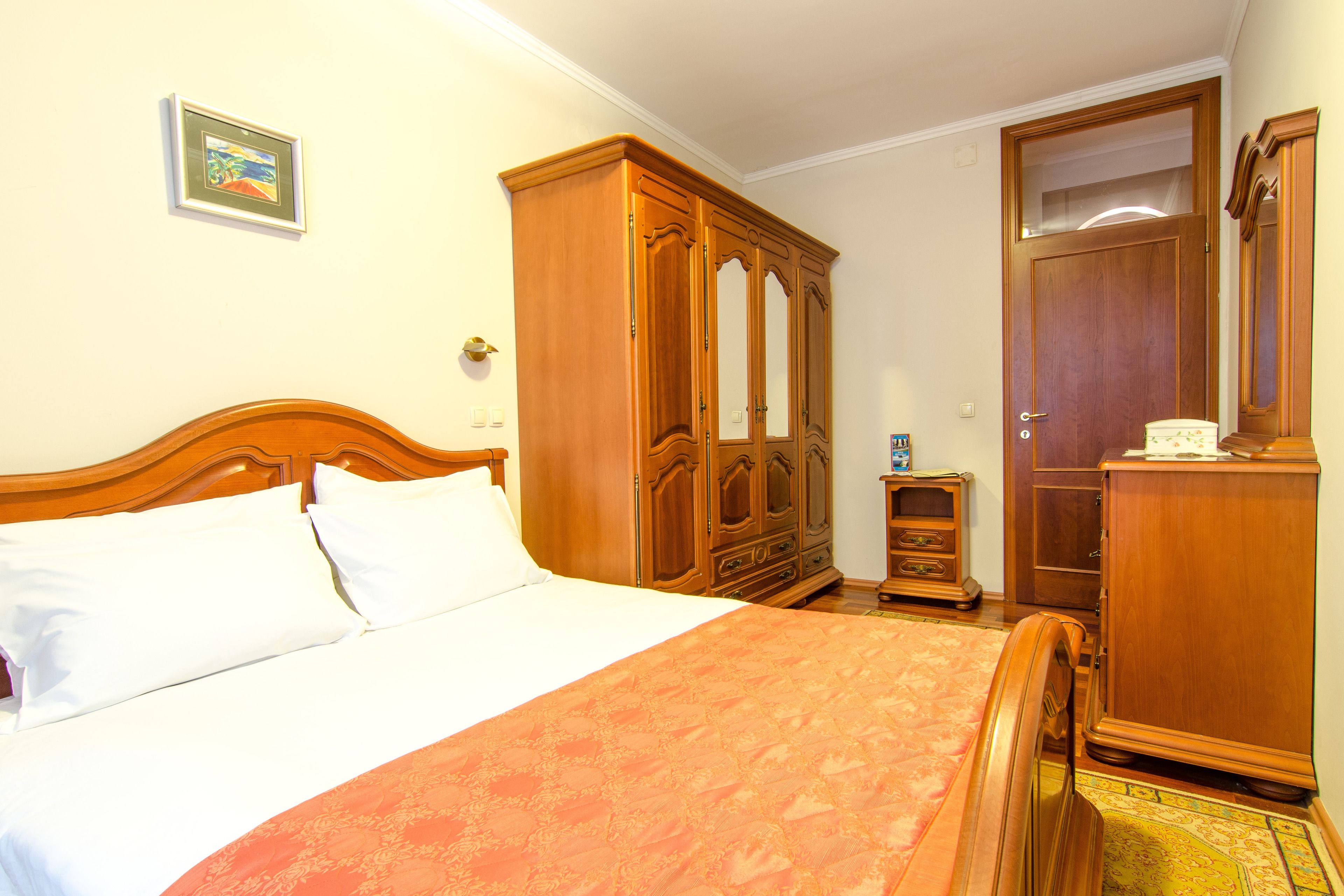 A hotel room with a wooden bed, a wardrobe, a small cabinet, and a mirror.