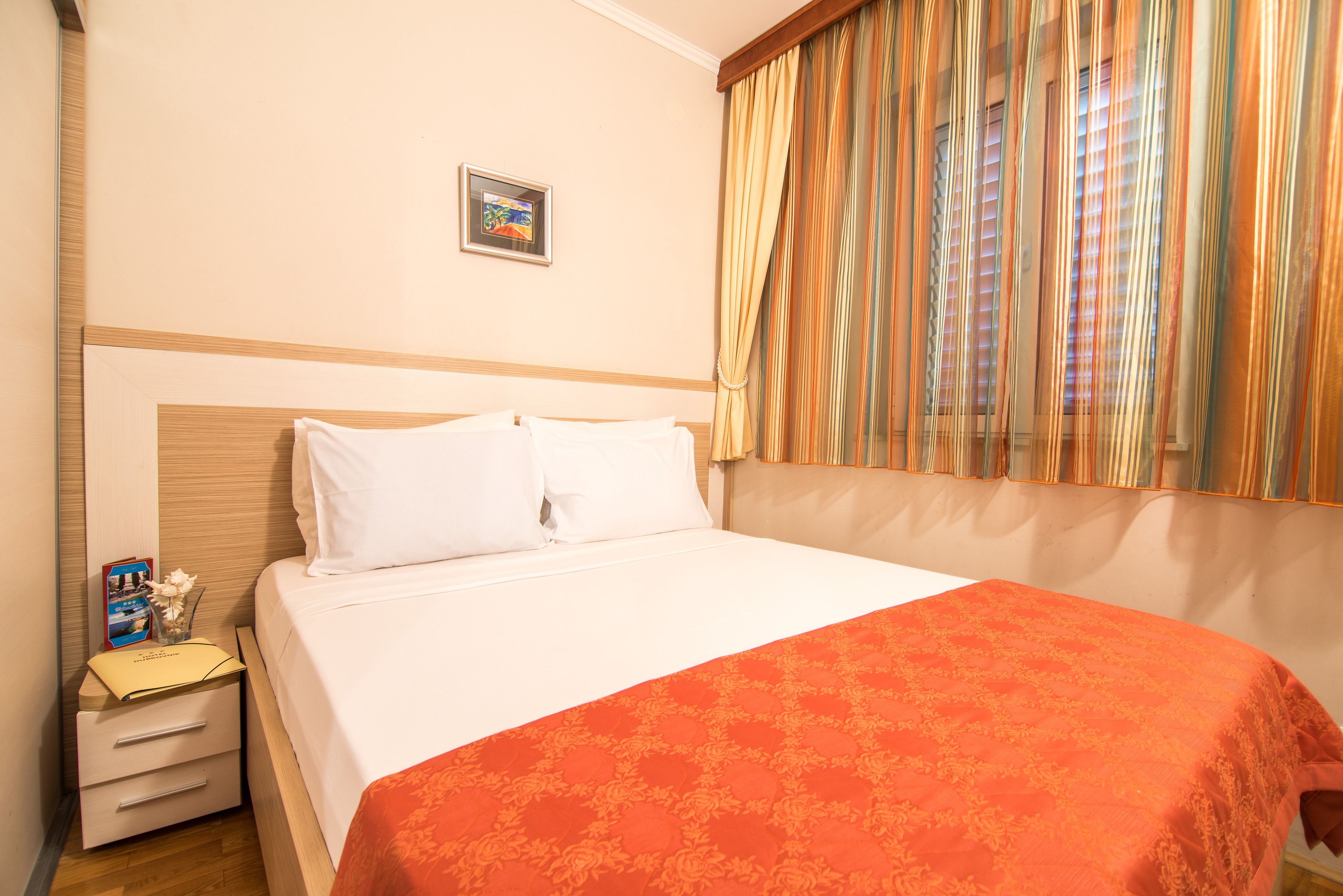 A hotel room with a neatly made bed, a bedside table with a lamp, and a window with curtains.