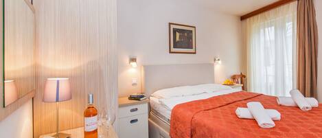 A hotel room with a bed, bedside table, lamp, phone, and a bottle of wine.