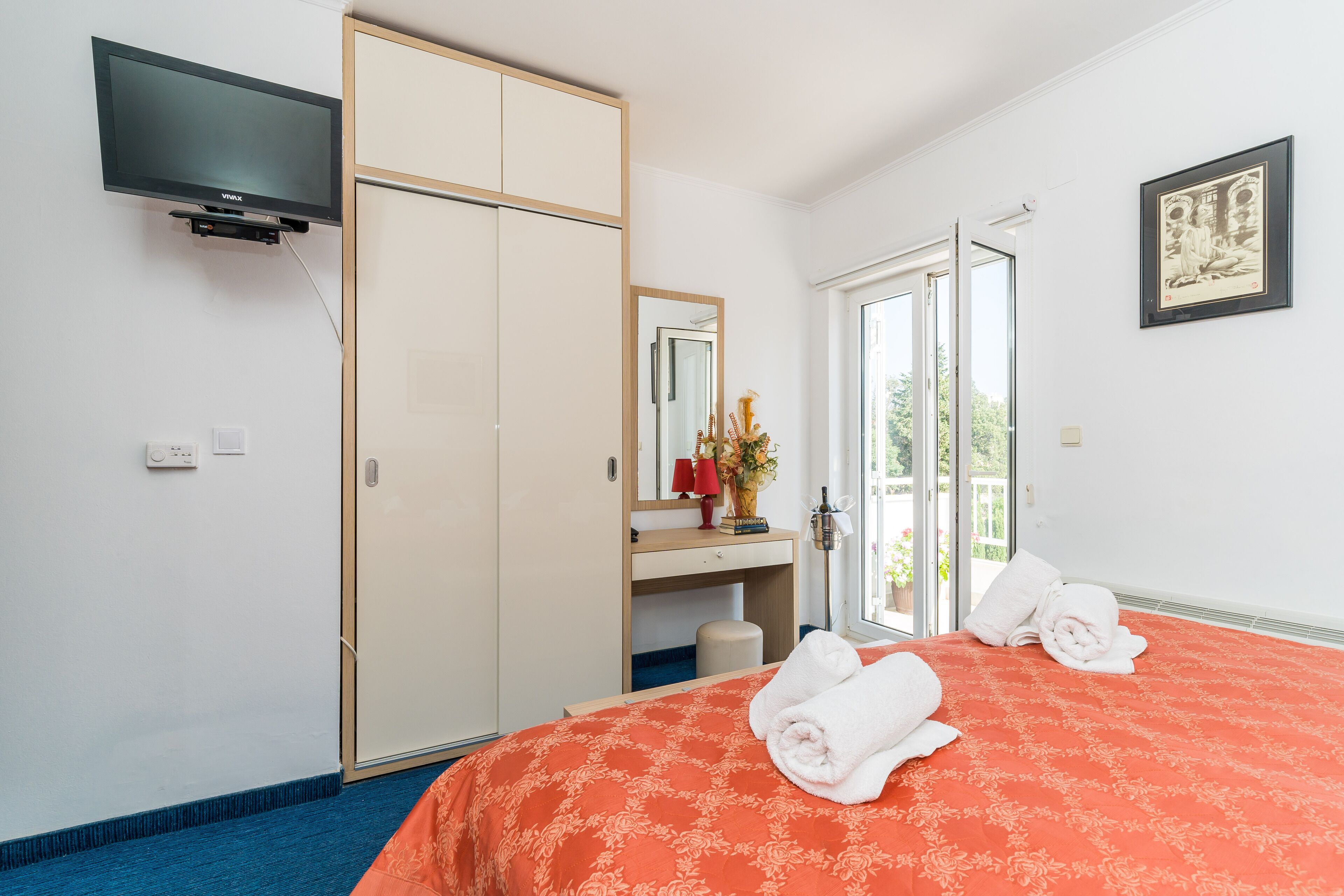 Habitación de hotel con una cama, televisor montado en la pared, armario, escritorio con espejo y ventana con vistas.