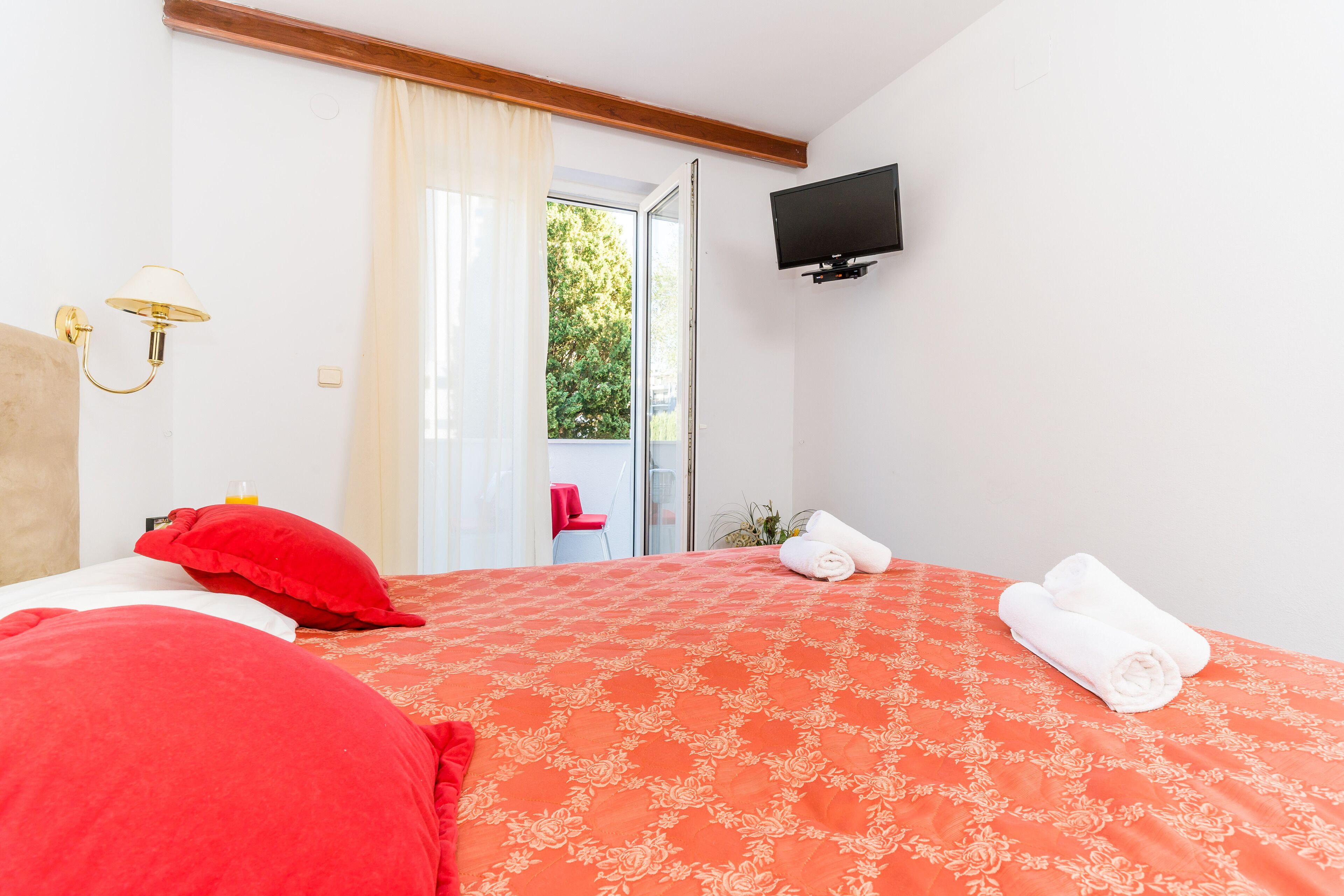 A hotel room with a bed, a television mounted on the wall, and a window with curtains.