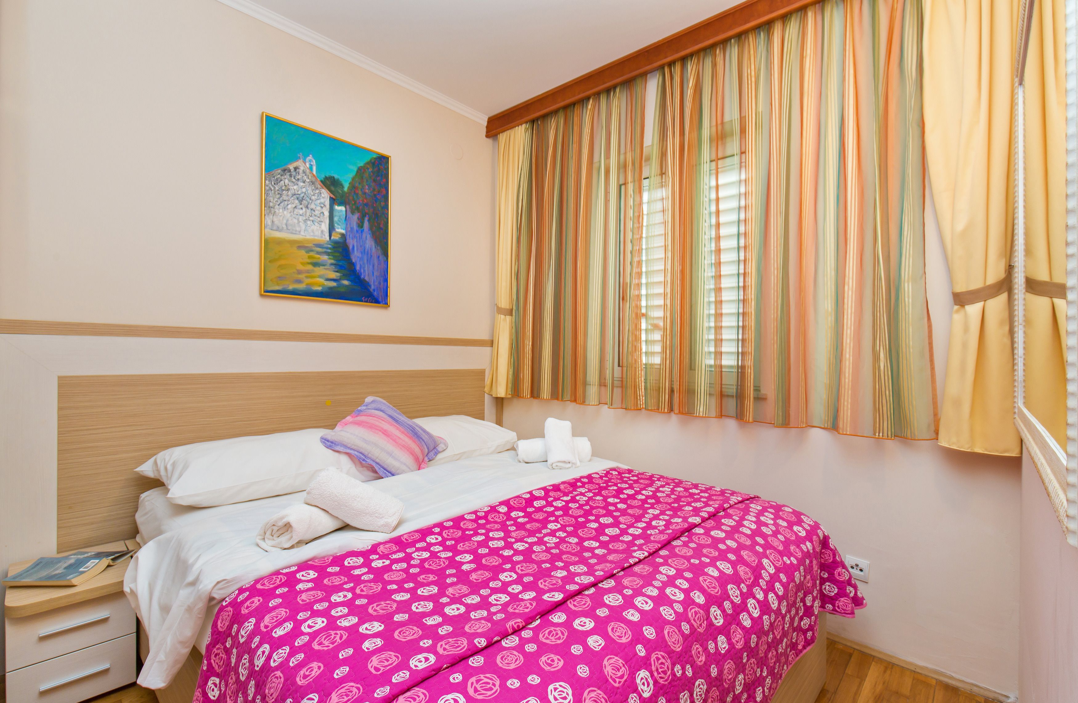A bedroom with a bed, pillows, a painting on the wall, and curtains.
