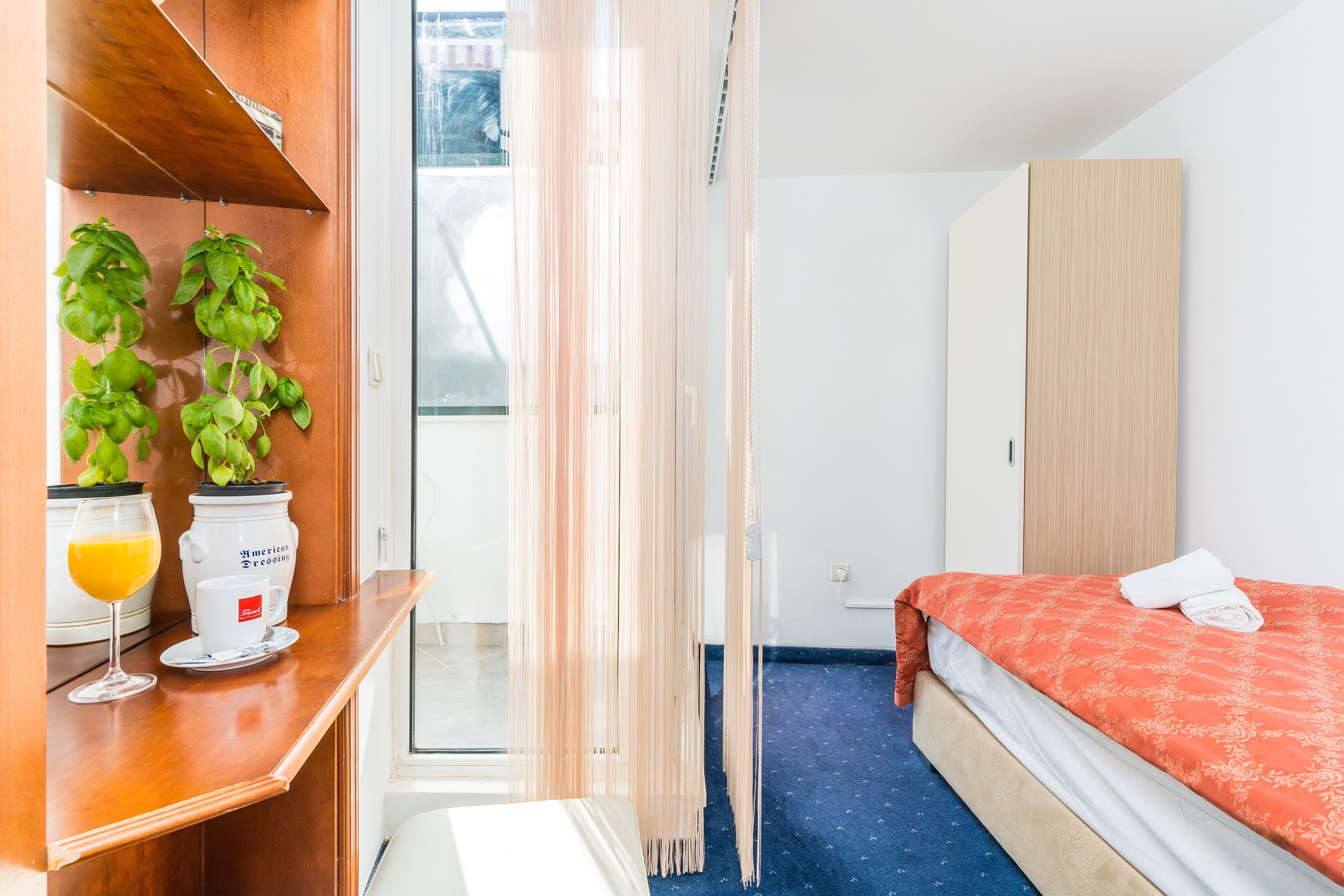 Hotelkamer met een bed, een houten garderobe, een tafeltje met een glas sinaasappelsap en een koffiekop, en een kamerplant.