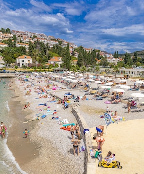 A crowded beach with people sunbathing and swimming, umbrellas, and beach chairs. - Hotel Dubrovnik (Dubrovnik)