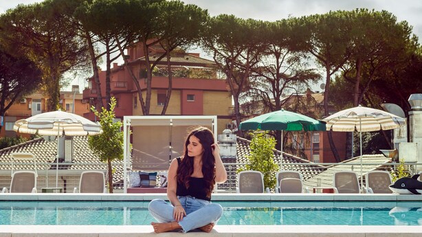 Zona de piscina con sillones, sombrillas y una piscina.
