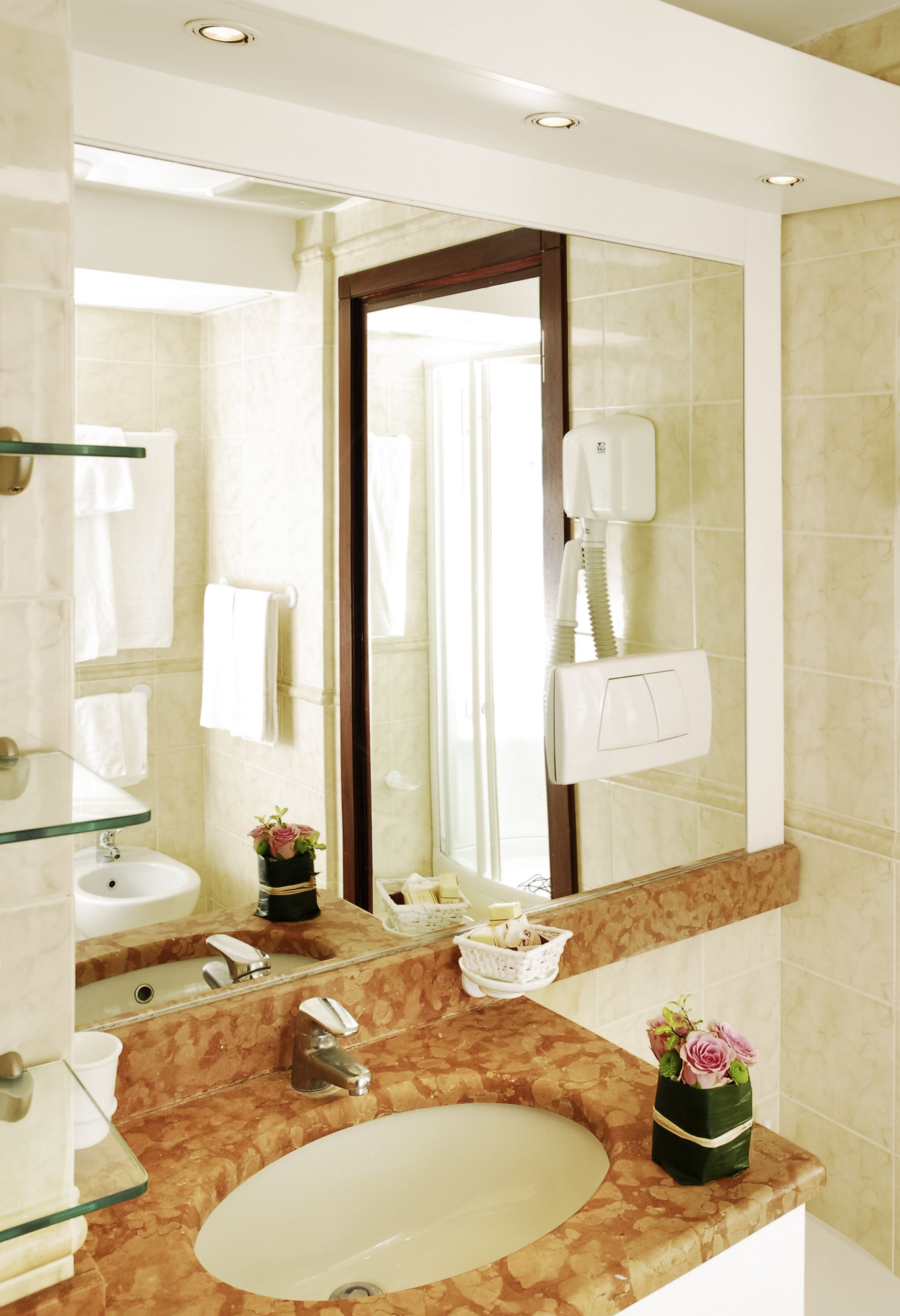 Une salle de bain avec un lavabo en marbre, une étagère en verre, un miroir, un porte-serviettes et un sèche-cheveux.