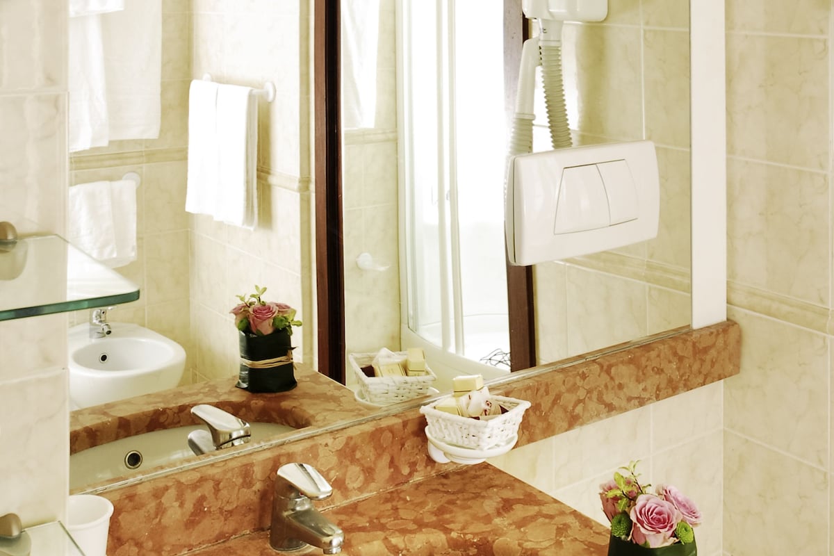 Une salle de bain avec un lavabo en marbre, une étagère en verre, un miroir, un porte-serviettes et un sèche-cheveux.
