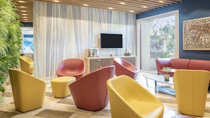 Un espace de détente moderne doté d’un téléviseur à écran plat, de sièges confortables et d’une grande fenêtre offrant une vue sur l’extérieur.