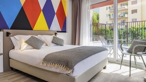 Habitación de hotel con una cama grande, un balcón con mobiliario exterior y un diseño de pared geométrico y colorido.