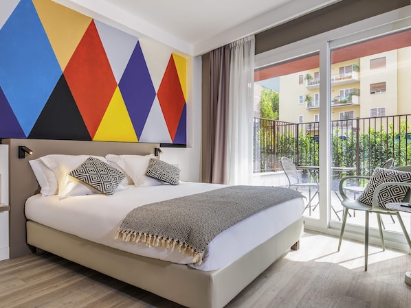 A hotel room with a large bed, a balcony with outdoor seating, and a colorful geometric wall design.