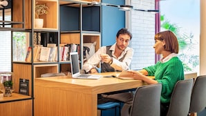 Une bibliothèque moderne avec des étagères en bois, un ordinateur portable sur un bureau et une personne qui lit un livre.